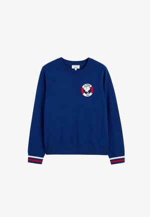 Maglione blu lavorato a maglia con scollatura rotonda, caratterizzato da un patch con logo al centro e polsini a righe rosse e bianche. Tessuto morbido.