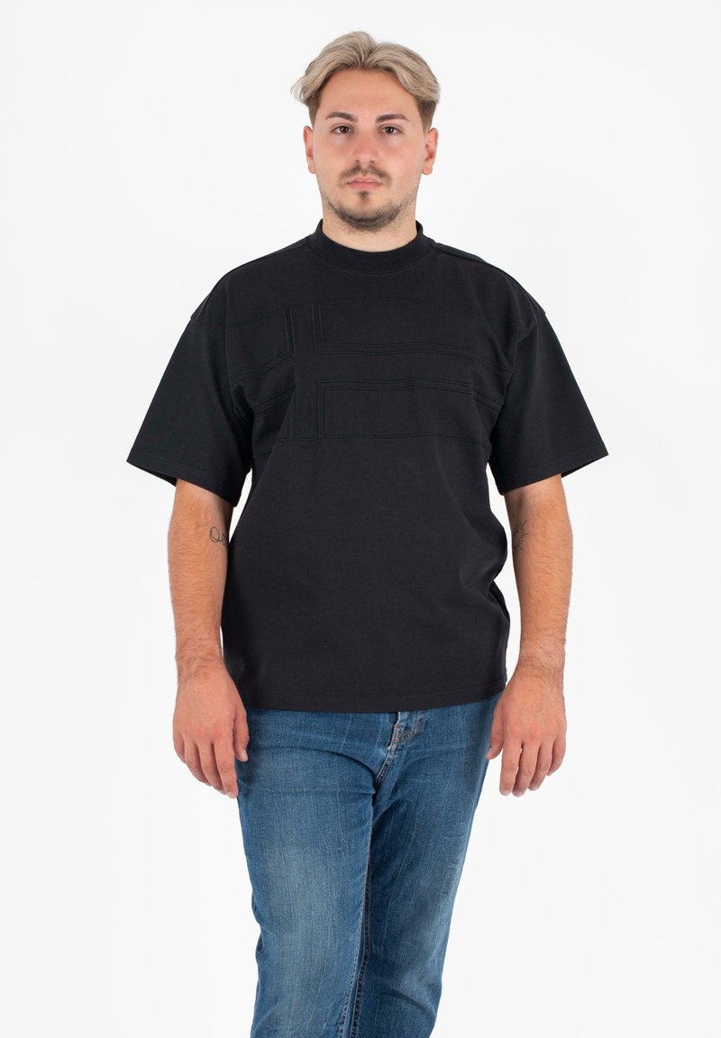 Zwarte t-shirt met korte mouwen en een ronde halslijn, versierd met getextureerde rechthoekige patronen aan de voorkant, gedragen met blauwe spijkerbroek.
