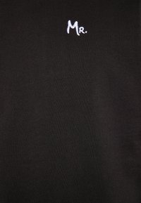 Sort bomulds T-shirt med hvid broderet tekst "Mr." placeret på venstre øverste side. Glat tekstur med en klassisk pasform.