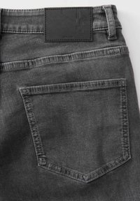 Retro posteriore di jeans in denim grigio scuro con bordi cuciti e un'etichetta in pelle nera del marchio sopra la cintura.