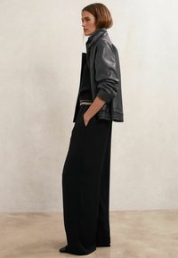 Mustast nahast jakk tekstuurse viimistlusega, kombineeritud musta kootud topiga ja laiade säärega mustade pükstega. Lihtne siluett ja elegantne disain.