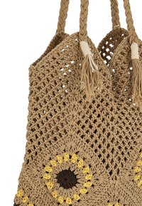 Flettet taske i naturfibre med en beige farve, med et solsikkemønster i gul og brun, pyntet med kvaster.