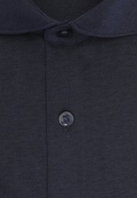 Gros plan sur le devant d'une chemise gris foncé avec un col et deux boutons visibles, un près du col et un en dessous.