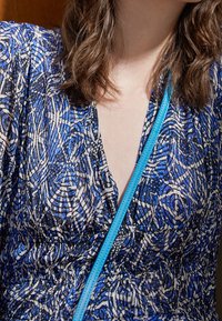Vestido azul y negro con un estampado y un escote en V, con cintura elástica. Una correa azul claro de un bolso cruza sobre la tela. Detalles de diseño texturizado.