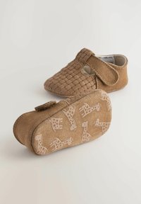 Chaussures pour bébés en daim marron avec un design supérieur tissé et une sangle Velcro ; la semelle présente un motif de girafes dans une teinte plus claire.