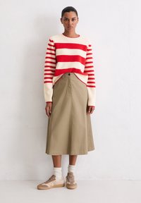 Pull en tricot rayé rouge et blanc, jupe évasée kaki, baskets beiges avec des accents texturés, et chaussettes blanches côtelées.