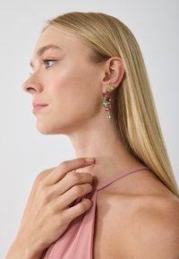 Kleurrijke hangoorbellen met groene en roze edelstenen, met een bloemontwerp en verschillende vormen, bevestigd aan een goudkleurige setting.