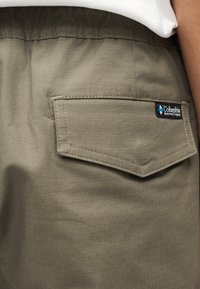 Τα χακι σορτς διαθέτουν πίσω τσέπη με χαρακτηριστική τριγωνική κλείστρα, ραμμένες λεπτομέρειες και ετικέτα με το λογότυπο της Columbia. Λείο, ελαφρύ ύφασμα.