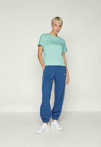 Lys teal kortermet T-skjorte med abstrakt design og blå joggebukser med hvite sidestriper, kombinert med hvite joggesko.
