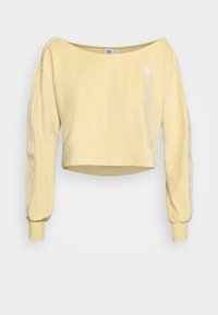 Gul beskuren sweatshirt med långa, puffiga ärmar, tre vita ränder på varje ärm och en liten vit logotyp på bröstet. Mjuk textur.