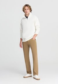 Maglione bianco a mezza zip con maniche lunghe, abbinato a pantaloni dritti beige e sneakers bianche. Design semplice e pulito senza motivi visibili.