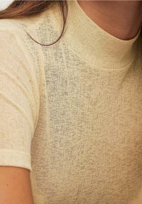 Hellgelbes, geripptes Stricktop mit hohem Ausschnitt und kurzen Ärmeln, das mit einem strukturierten Stoff für zusätzlichen visuellen Reiz versehen ist.