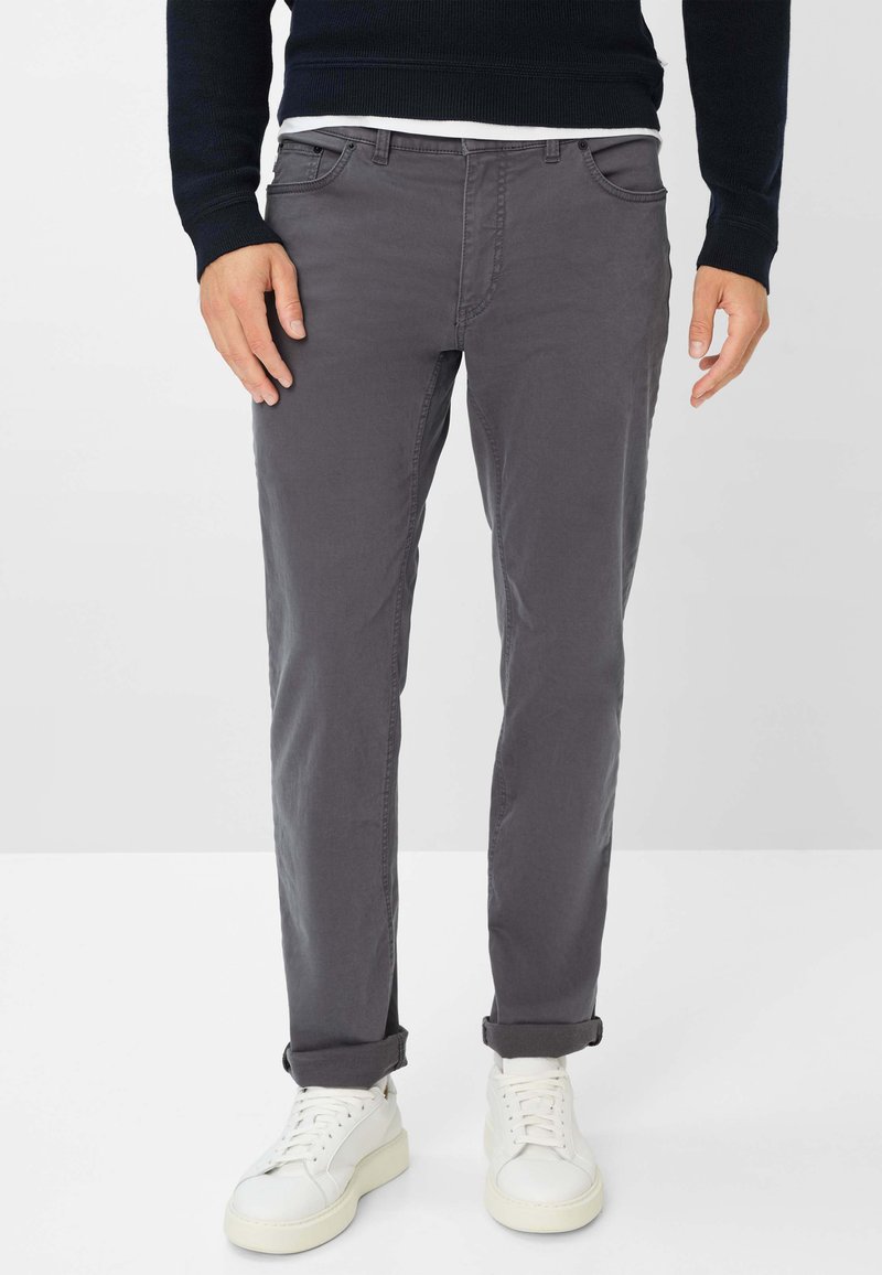 Pantaloni in cotone grigi con vestibilità slim, caratterizzati da orli arrotolati, tasche frontali e un design pulito, abbinati a sneaker bianche.