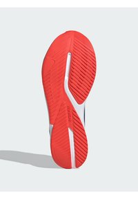 Sole di scarpa atletica rossa e bianca con gomma testurizzata, caratterizzata da scanalature diagonali e il marchio "ADIDAS" in lettere in rilievo.