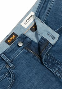 Dunkelblå denimjeans med dragkedja, knappstängning och flera etiketter inuti, inklusive "BOSS" och "Soft Motion."