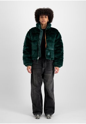 Jachetă puffer din blană sintetică verde, cu guler înalt, închidere cu fermoar și căptușeală portocalie în contrast. Purtați-o cu blugi negri cu picior larg și adidași.