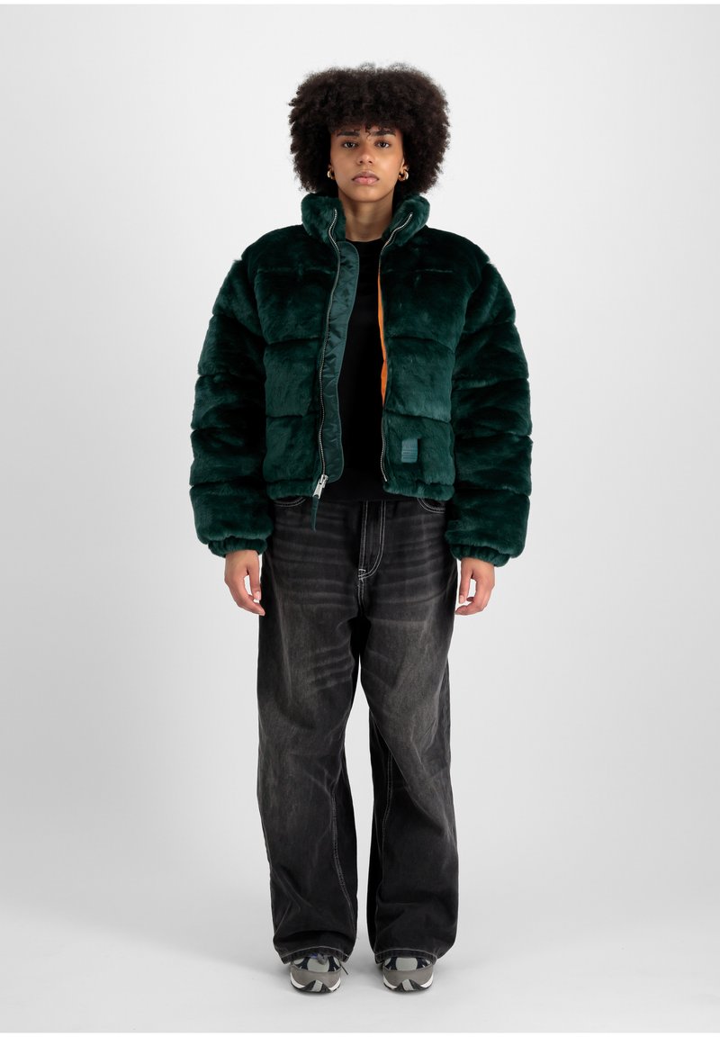 Jachetă puffer din blană sintetică verde, cu guler înalt, închidere cu fermoar și căptușeală portocalie în contrast. Purtați-o cu blugi negri cu picior larg și adidași.