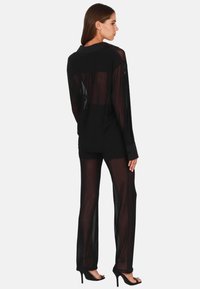 Schwarzes, transparentes Langarmshirt und passende Hose, beide aus leichtem, durchsichtigen Stoff. Maßgeschneiderter Schnitt mit Knopfmanschetten und offenem Rücken.