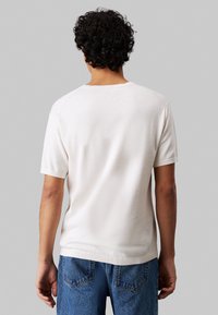 T-shirt bianco in cotone a maniche corte con colletto a giro, polsini a costine e vestibilità rilassata, abbinato a jeans denim blu.