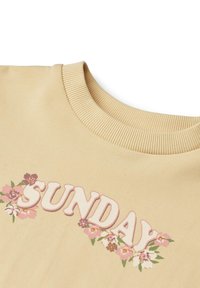 Krämfärgad sweatshirt med ribbad krage, med "SUNDAY" i rosa och blommiga detaljer i lila och rosa runt texten.