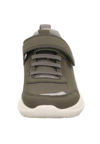 Grüner Sportschuh mit strukturiertem Obermaterial, reflektierenden Akzenten, elastischen Schnürsenkeln und einem Klettverschluss. Hat eine runde weiße Sohle.