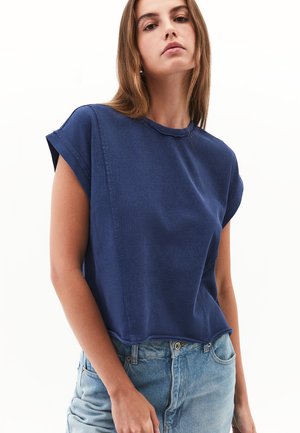 Chemise à manches courtes bleu marine avec une coupe droite, détails de couture visibles et un col rond, associée à un jean taille haute bleu clair.