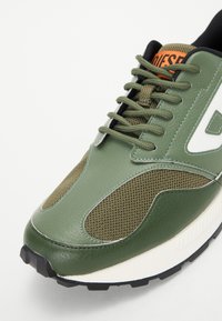 Grønn sneaker med skinn- og nettingmaterialer, snøring, kraftig svart gummisåle og kontrasterende hvite accenter.