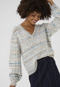 Vaatteet: Neule beige ja sininen V-kaula-aukko, jossa on pitkät, puffattuja hihoja. Teksturoitu pinta ja väljää istuvuutta. Yhdistetty tummaan farkkuhameeseen.