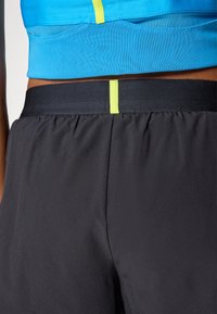 Svarte treningsshorts med elastisk midje og lyse gul detaljer. Toppene er en blå crop top med teksturert design.