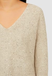 Maglione beige lavorato a maglia con scollo a V, caratterizzato da un motivo testurizzato e paillettes sparse per un tocco di originalità. Tessuto morbido e vestibilità comoda.