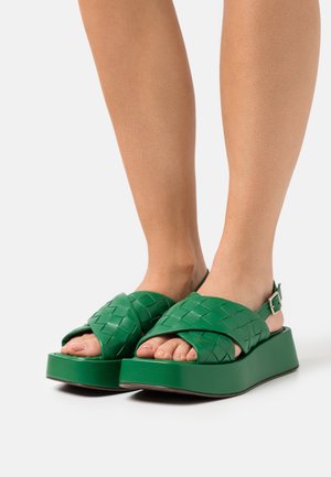 Sandali platform intrecciati verdi con design a incrocio, suola spessa, cinturino alla caviglia regolabile e texture liscia.