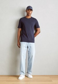 Marinblå kortärmad t-shirt, ljusblå jeans, vita sneakers och en grå keps. Enkel, avslappnad design med en logotyp på bröstet av t-shirten.