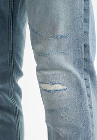 Jeans in denim blu sbiadito con aree delle ginocchia strappate. Bordo sfilacciato visibile e lavaggio chiaro, con dettagli di cucitura lungo le cuciture.