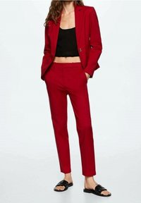 Veste de costume rouge cintrée à un seul bouton, associée à un pantalon slim assorti et un top en maille noir court. Comprend des sandales à glissière noires.