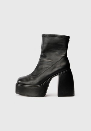 Botas de tornozelo em couro preto com bico arredondado, textura suave e um salto bloco proeminente. Apresenta um fecho lateral. Design minimalista.