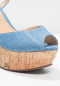 Sandale compensée avec dessus en denim bleu clair et semelle plateforme en liège, avec bout ouvert et bride à la cheville.