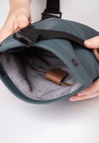 Teal leather bag with a gray checked interior. Features a brown leather strap inside. Contains a buckle and adjustable strap.