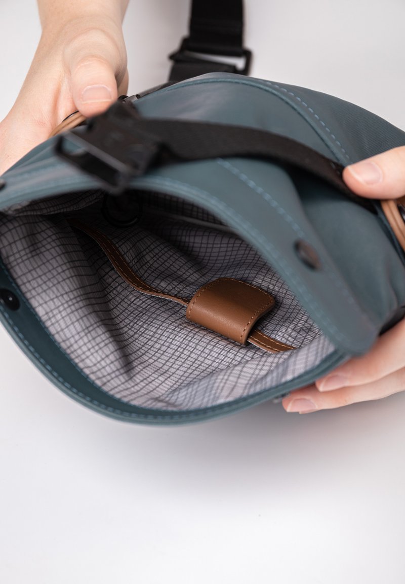 Teal leather bag with a gray checked interior. Features a brown leather strap inside. Contains a buckle and adjustable strap.