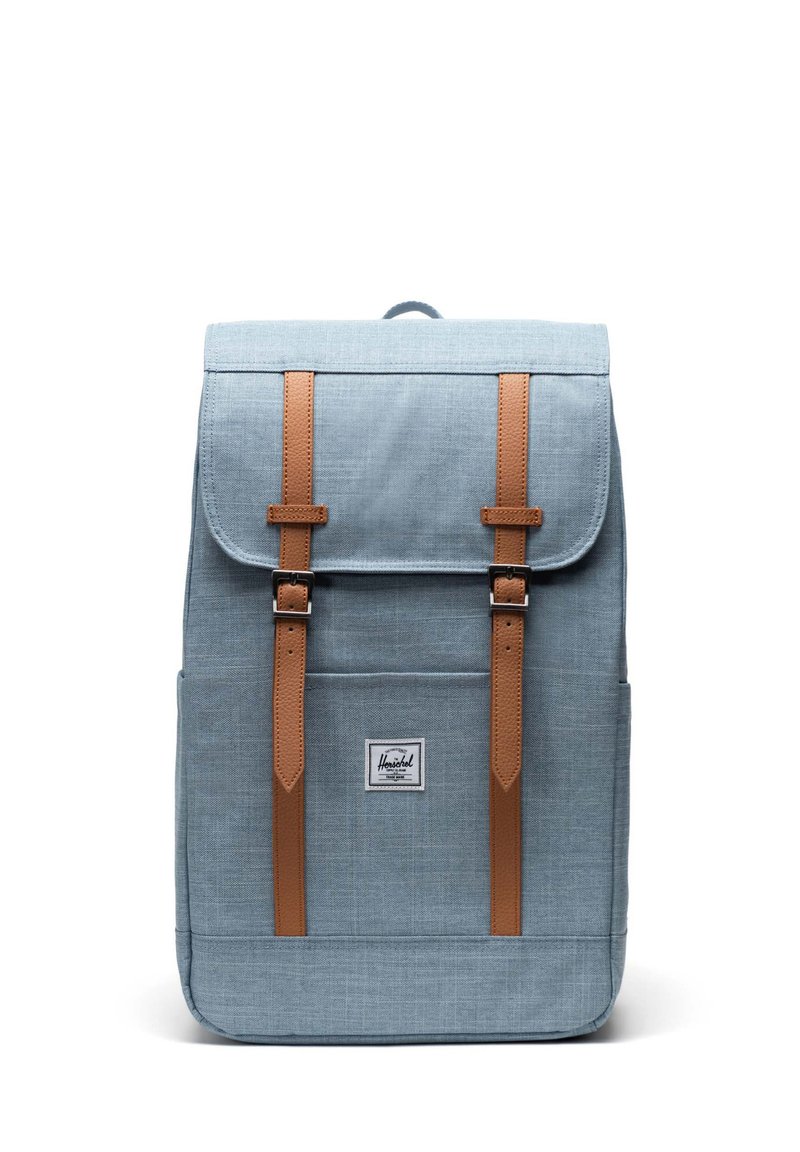 Light blue fabric backpack with brown leather straps and accents, featuring a flap closure and a front label logo. Classic rectangular shape.