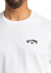 White cotton t-shirt with a crew neckline, featuring a black embroidered "Billabong" logo on the chest area.