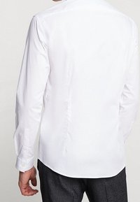 Uomo visto di spalle che indossa una camicia bianca a maniche lunghe e pantaloni grigio scuro.