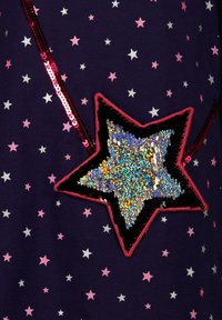 Dunkles Gewebe mit verstreuten pinkfarbenen und silbernen Sternen, das einen großen glänzenden multicolor Paillettenstern mit schwarzer und roter Umrandung zeigt.
