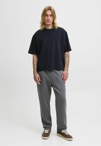 Czarna, oversize koszulka z krótkim rękawem, szare dresy i brązowe sneakersy z białymi sznurówkami, stojąca na białym tle.