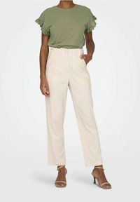 Olivgrön kortärmad topp med volangkant, tillsammans med högmidjade byxor i krämfärgad nyans. Minimalistisk design och mjuk textur.