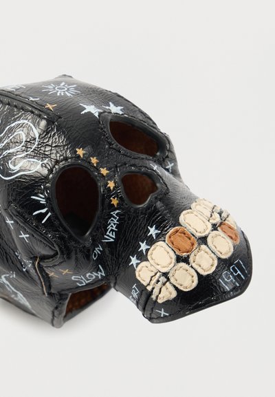 Μάσκα κρανίου από μαύρο δέρμα με ανοίγματα για τα μάτια, ραμμένα δόντια σε μπεζ και καφέ, με λευκά και ασημί διακοσμητικά σχέδια.