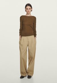 Brown long-sleeve knit top with a boat neck; paired with beige wide-leg trousers featuring front pleats and a relaxed fit. Black footwear.