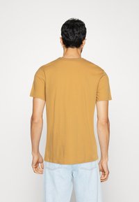 T-shirt à manches courtes en coton jaune moutarde, design ajusté, col rond, texture lisse, présenté de dos.