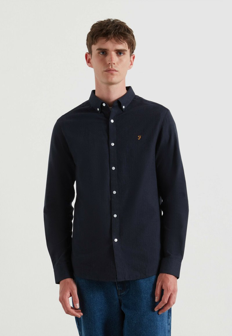 Camicia a maniche lunghe blu navy con colletto a bottone, caratterizzata da bottoni bianchi e un piccolo logo arancione sul petto. Tessuto texture.
