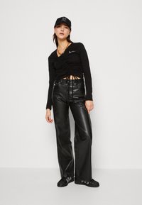 Sort langærmet top med samlet frontdesign, med højmidte sorte bukser i faux læder og sorte sneakers med hvide striber.