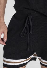 Pantaloni corti neri in maglia con un tessuto testurizzato, vita elastica con stringi e strisce orizzontali a contrasto in bianco e marrone.